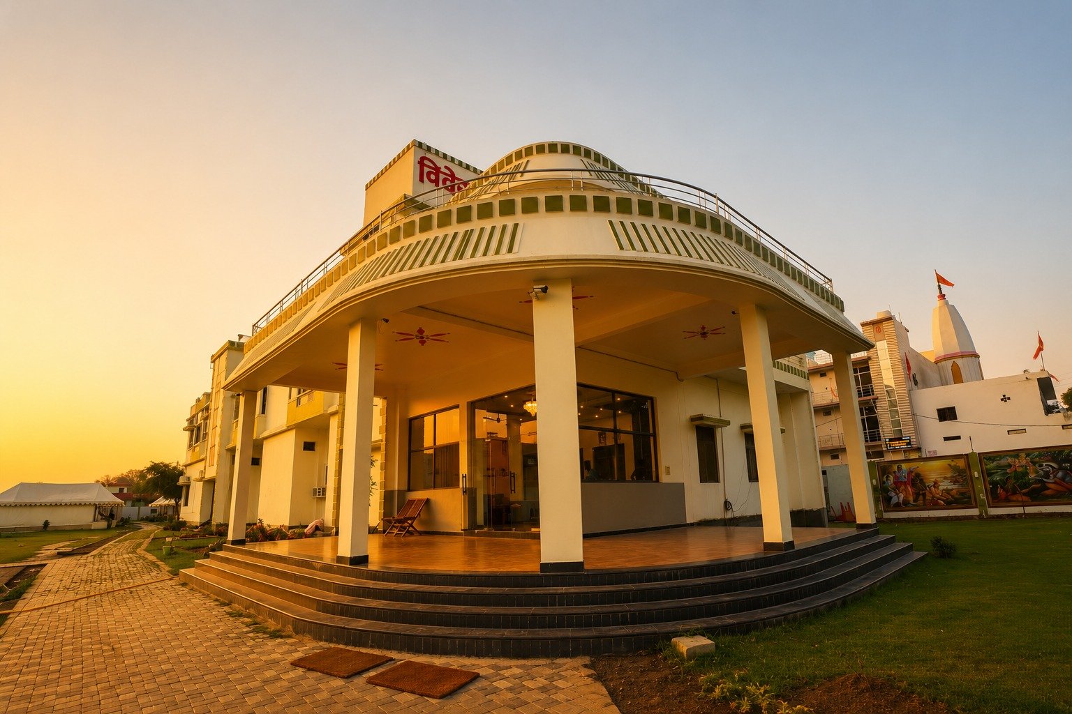White modern pavilion with a curved, tiered roof and glass-front entrance, bathed in golden sunset light.