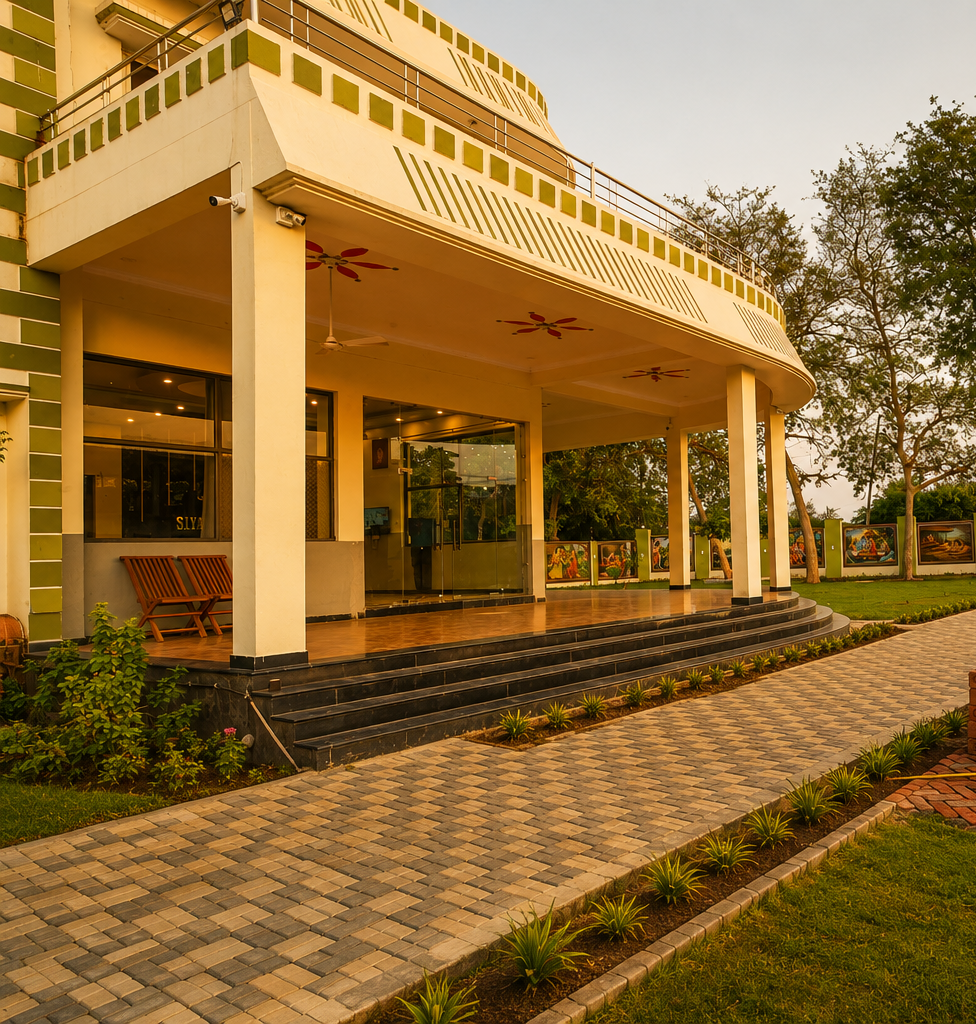 Modern white building with a curved veranda, glass doors, and black tiled steps, surrounded by a brick-paved path and landscaped lawn.